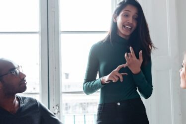 Une manager donne un feedback constructif à deux collègues lors d'une réunion dans un cadre collaboratif