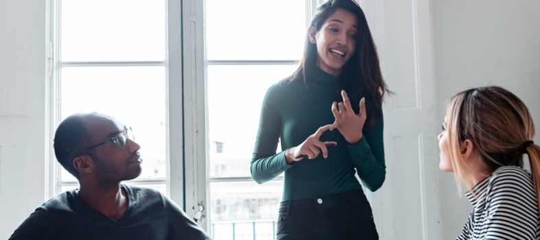 Une manager donne un feedback constructif à deux collègues lors d'une réunion dans un cadre collaboratif