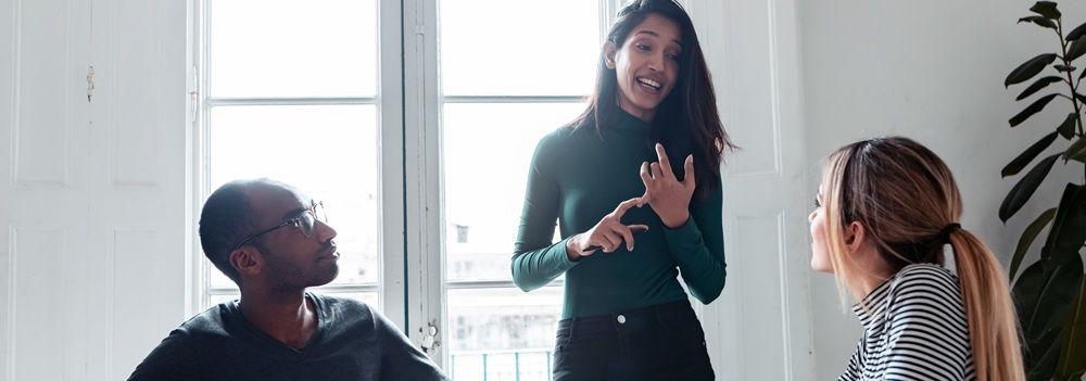 Une manager donne un feedback constructif à deux collègues lors d'une réunion dans un cadre collaboratif